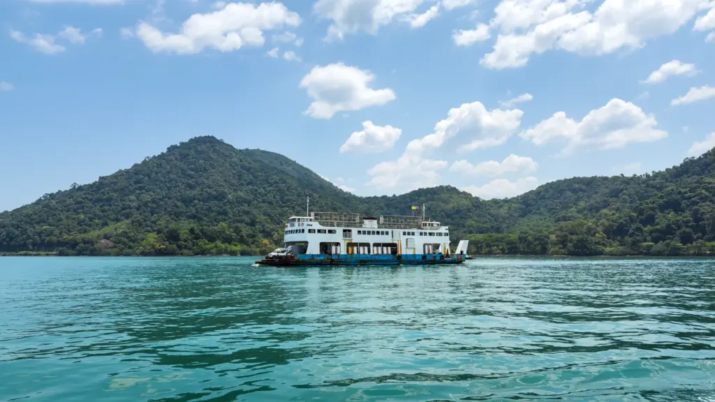 Vehicle ferry crossing tropical water between green islands in southern Thailand